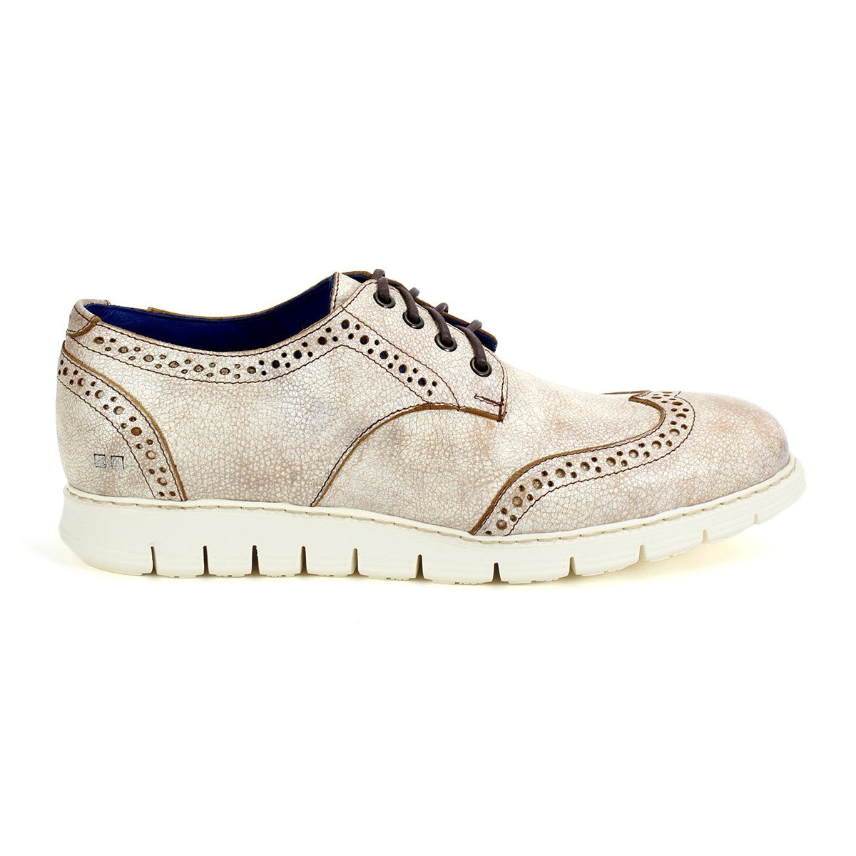 The Bed|Stü Cayuga II is a light beige suede wingtip shoe featuring classic brogue detailing, dark brown laces, and a thick white rubber sole, shown in profile view.