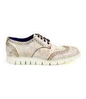 The Bed|Stü Cayuga II is a light beige suede wingtip shoe featuring classic brogue detailing, dark brown laces, and a thick white rubber sole, shown in profile view.