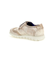The Bed|Stü Cayuga II is a beige leather derby shoe in a wingtip style, showcasing classic brogue perforations, dark laces, and a white sole, displayed at an angle on a white background.