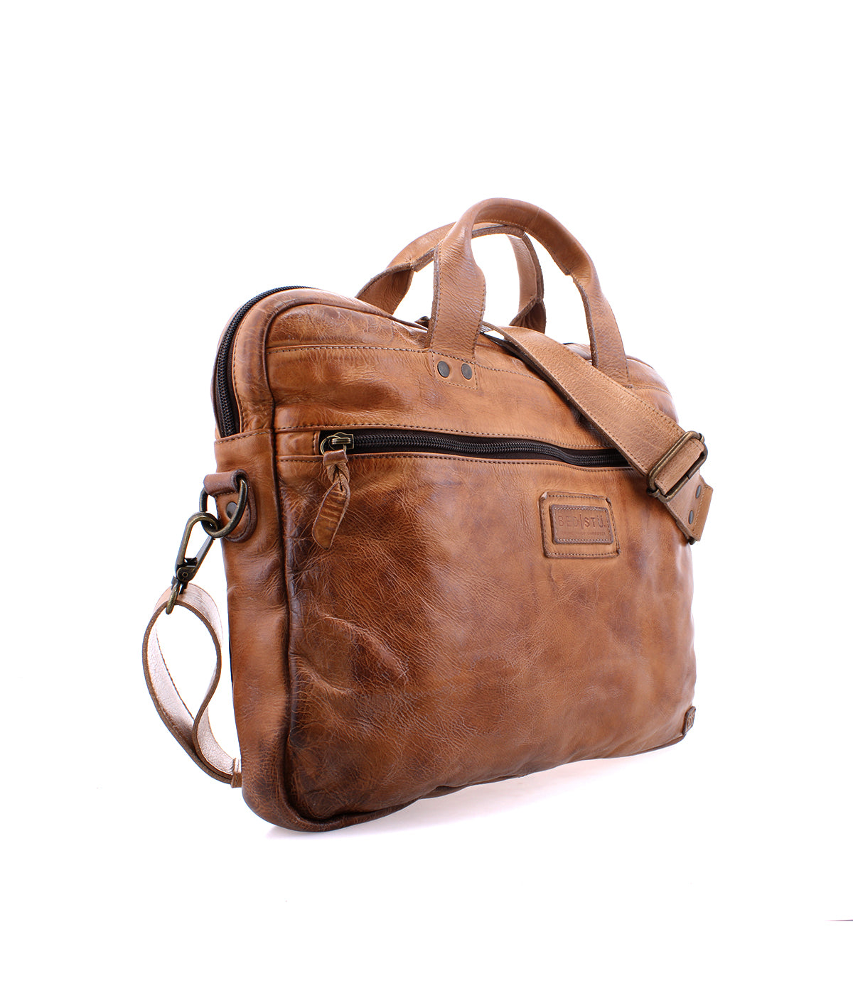 The Bed|Stü Conclusion is a brown leather messenger bag expertly crafted from premium vegetable-tanned leather. It features a zipper pocket, top handles, and an adjustable shoulder strap. Designed with a dedicated laptop section for added convenience, this briefcase is displayed on a white background.