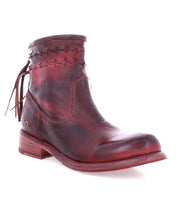 The Craven by Bed|Stü is a red-brown leather ankle boot featuring decorative stitching, a woven shaft detail, side tassels, and a wooden heel. Shown on a white background, its hand-finished leather adds depth to the design, while the unique fringe heel adds playful movement with every step.