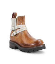 Introducing the Bed|Stü Daring ankle boots—crafted from brown leather with a low heel, featuring a black rugged sole and two white decorative straps adorned with silver buckles. These boots blend standout style with dependable durability, making them the ideal choice for everyday wear.