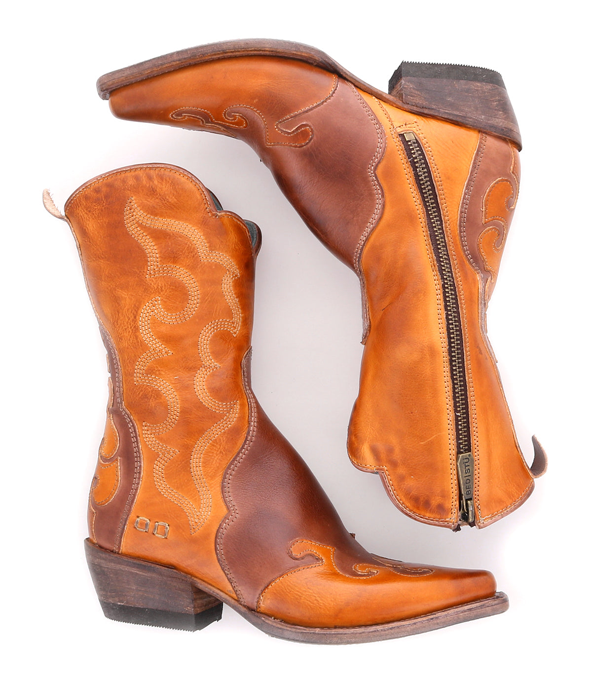 The Bed|Stü Deuce is a pair of mid-calf brown Western boots, crafted from vegetable-tanned leather with detailed stitching and convenient side zippers, shown against a white background.