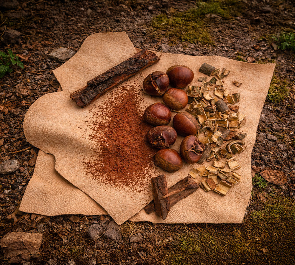 Natural tanning materials, including bark, chestnuts, wood chips, and reddish powder, arranged on pieces of light-colored leather outdoors.