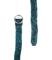 A close-up of the Bed|Stü Dreamweaver woven leather belt in teal and black, featuring a round silver buckle and laid out flat with the end extending upward. This accessory highlights artisan craftsmanship and adds a touch of bohemian style to any outfit.