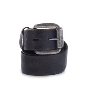 The Bed|Stü Drifter is a rolled-up black leather belt featuring a metal buckle, displayed against a white background to highlight its minimal style and textured leather strap.