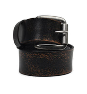 A well-worn Bed|Stü Drifter belt in black, featuring a distressed textured leather strap with visible scuff marks and a tarnished metal buckle, coiled neatly.