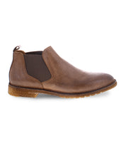 The Elude men's boots by Bed|Stü feature brown leather uppers, elastic side panels, a back pull tab, and a textured rubber sole. Displayed in side view against a white background, these slip-on Chelsea boots offer timeless style and comfort.