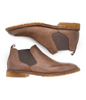 Introducing the Bed|Stü Elude — a pair of brown leather Chelsea boots featuring elastic side panels and crepe soles, displayed from the side and bottom. These slip-on men's boots blend comfort with sophistication, offering a timeless addition to any wardrobe.