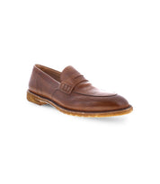 The Bed|Stü Envoy loafer is crafted from premium Italian brown leather and features a low heel, intricate stitched detailing, and a decorative strap across the upper. Handcrafted with care, these loafers boast a textured rubber sole for added grip and are beautifully displayed against a white background.