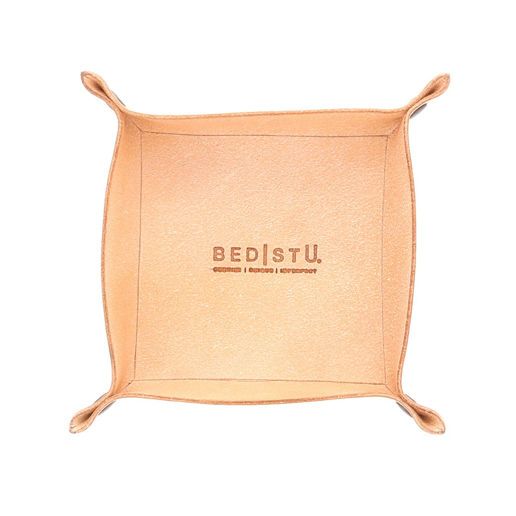The Expanse Catchall Tray by Bed|Stü is a square tan leather valet tray featuring raised edges and rounded corners, embossed with the "Bed|Stü" logo and additional small text below, shown on a white background—ideal for organizing your essentials.