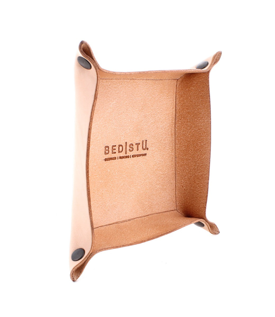The Expanse Catchall Tray by Bed|Stü features tan leather construction with black snap buttons at the corners and is embossed with "Bed|Stü" on the inside bottom surface. This stylish valet tray is perfect for organizing your essentials in any space.