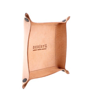 The Expanse Catchall Tray by Bed|Stü features tan leather construction with black snap buttons at the corners and is embossed with "Bed|Stü" on the inside bottom surface. This stylish valet tray is perfect for organizing your essentials in any space.