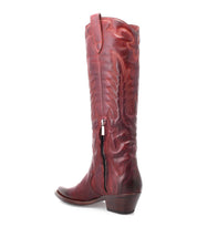 The Bed|Stü Finito is a tall brown leather cowboy boot featuring decorative stitching, a distressed finish, a side zipper, a low stacked heel, and a pull tab, shown from a side angle on a white background.