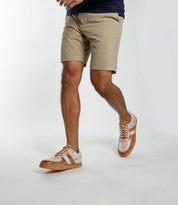 A man wearing beige shorts, a navy shirt, and Bed|Stü Firepower everyday sneakers—featuring leather stripe details and a textured sole—walks against a plain white background.