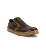 Freestyle by Bed|Stü is a brown leather slip-on sneaker with a tan sole, yellow trim, and blue inner lining, shown against a white background. This comfortable sneaker features stylish leather accents for a modern touch.
