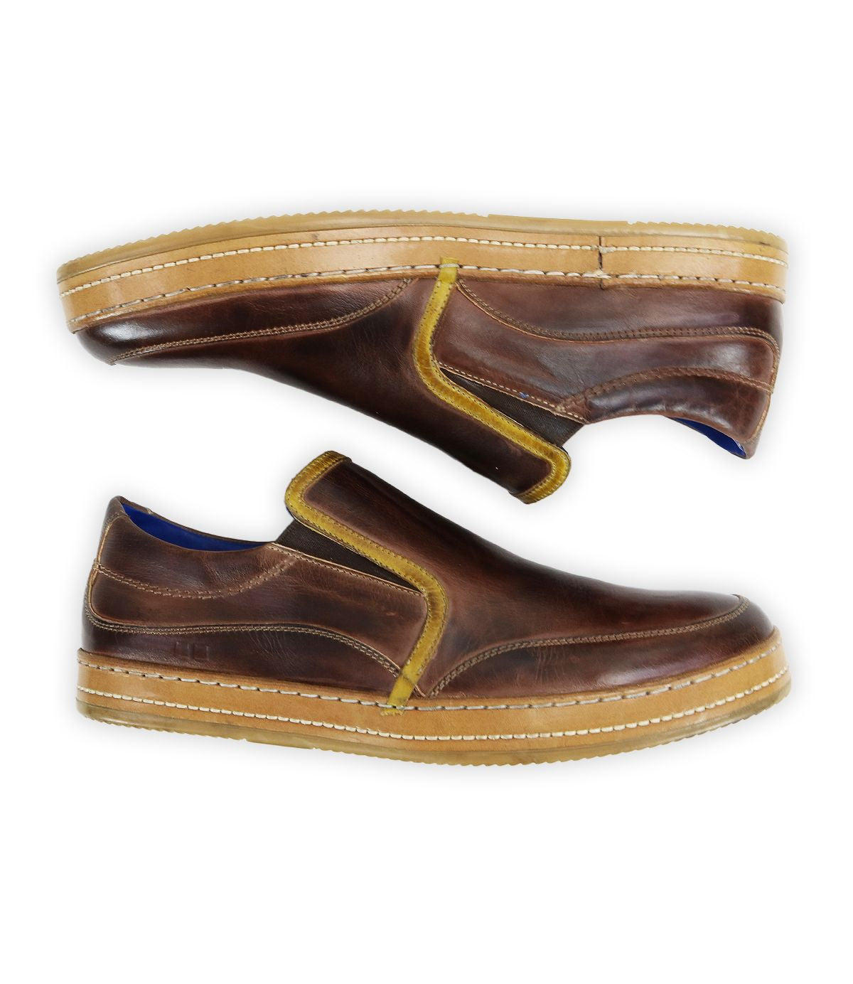 The Bed|Stü Freestyle features brown leather slip-on sneakers with yellow trim and tan soles, displayed in a side view with one shoe stacked on top of the other, providing a comfortable and stylish option for everyday wear.