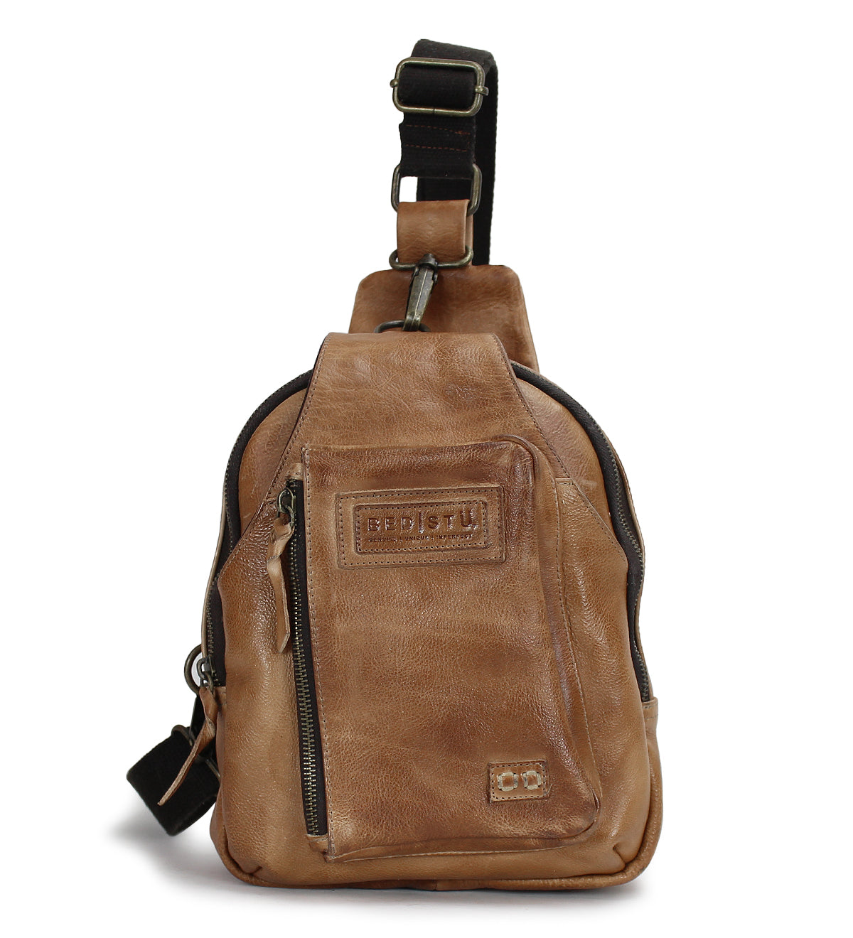 The Bed|Stü Beau is a small brown leather sling bag featuring a front zipper pocket and an adjustable black strap, shown standing upright to highlight its sleek yet practical design—an ideal choice for anyone seeking a compact alternative to a backpack.