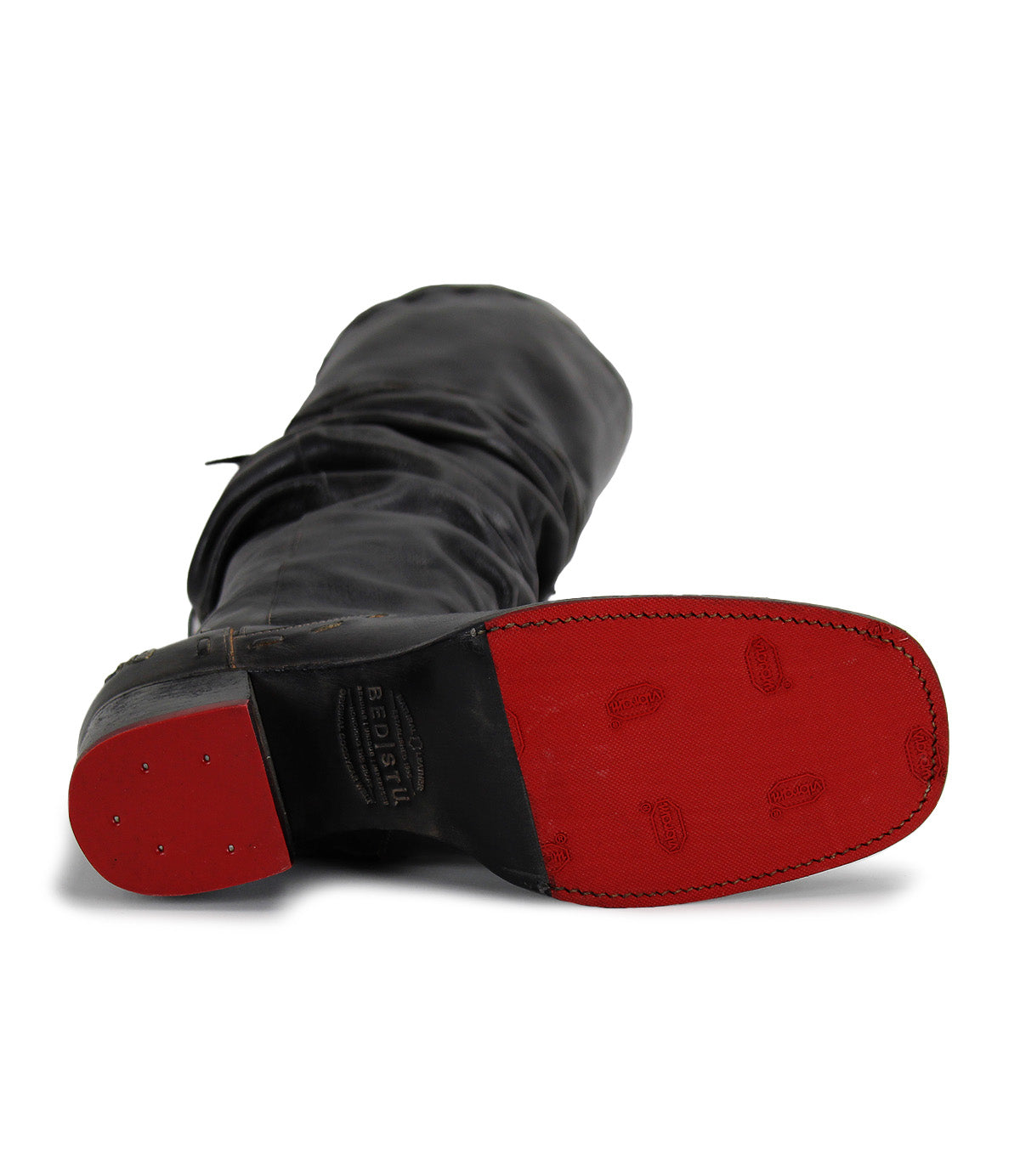The Leilani boot by Bed|Stü, crafted in black leather, lies on its side to reveal a red rubber sole accented with visible stitching and small metal studs at the heel; elegant ruching along the shaft adds texture, making this a true stand-out style.