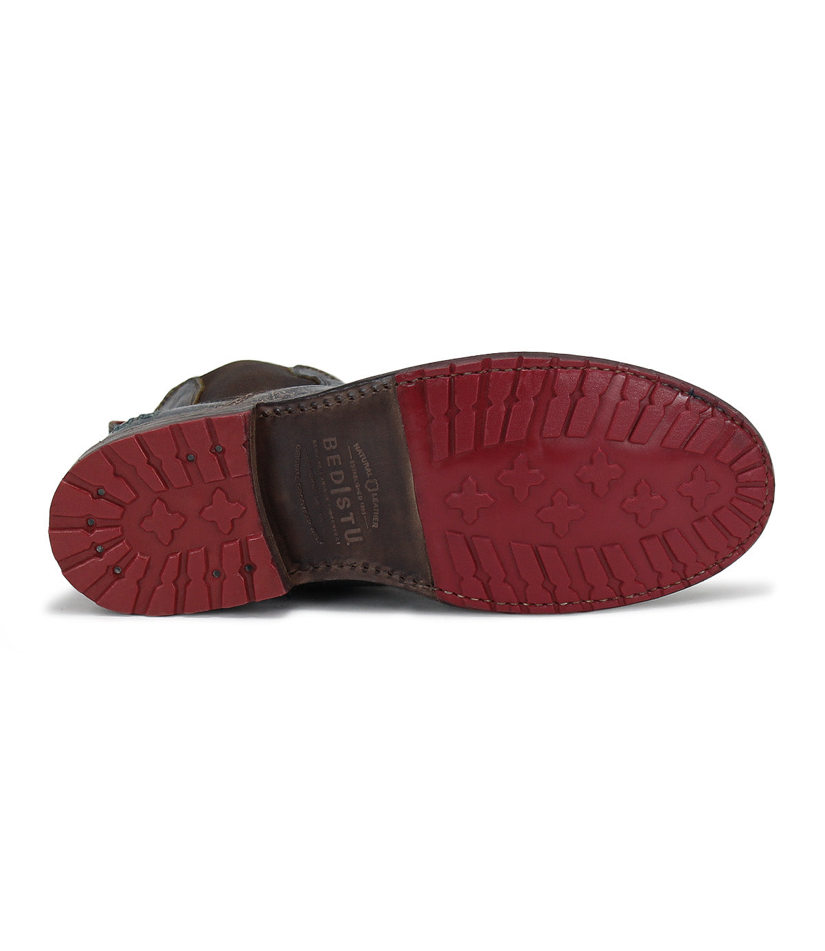 The image displays the bottom view of the Bed|Stü Nandi, a brown leather Chelsea boot with a red rubber sole designed with grooves and treads for enhanced grip, showcasing its versatile style and easy slip-on convenience.