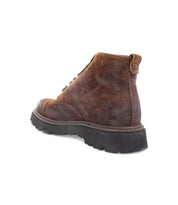 The Bed|Stü Goer is a brown oiled suede leather lace-up cap-toe boot with a rugged black sole, showcased from a back side angle against a white background and inspired by classic Italian work-style boot design.