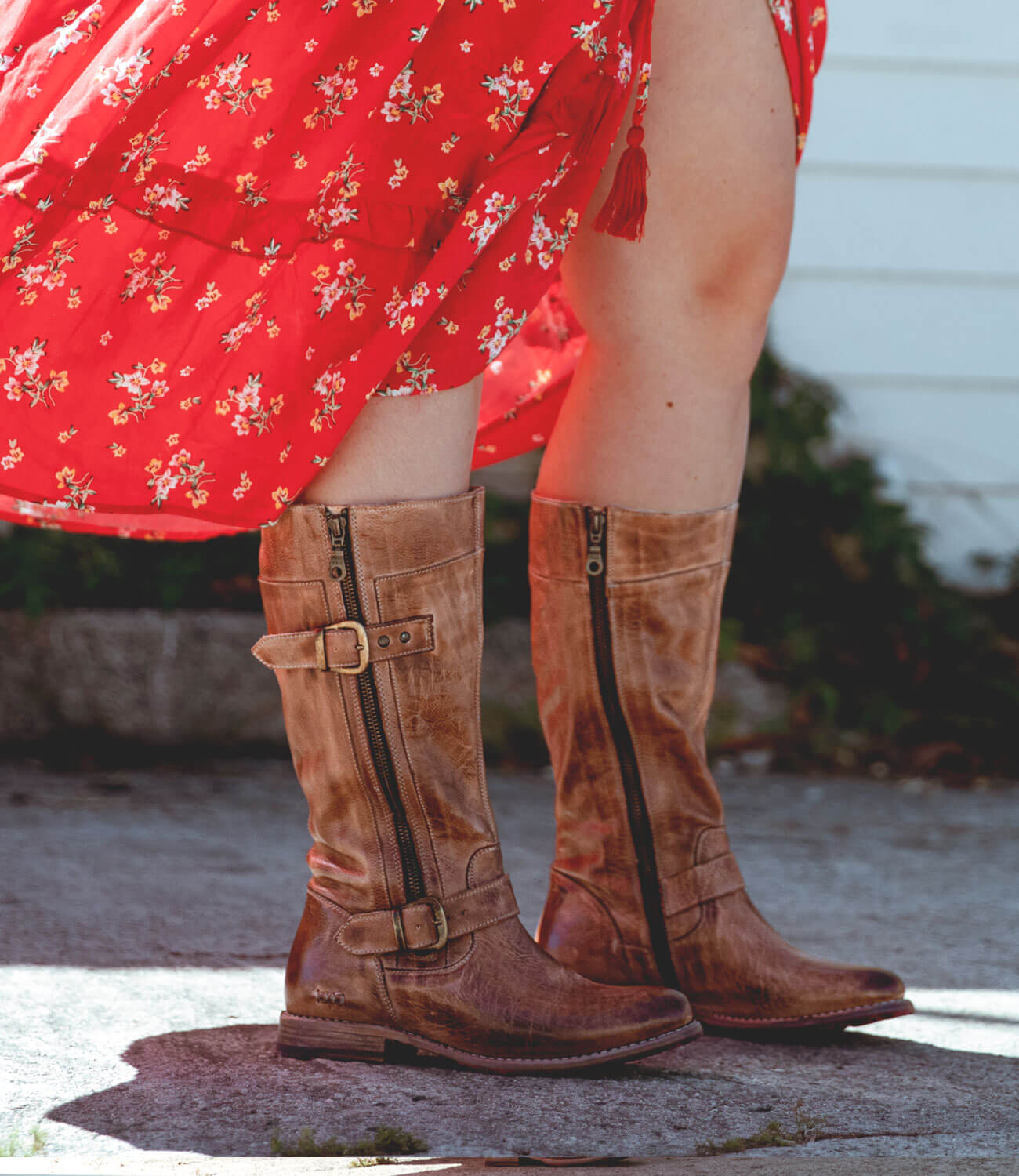 A person wearing a red floral dress and Bed|Stü Gogo Lug Wide Calf boots with zippers and buckles stands on a sidewalk.