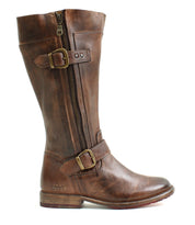 The Gogo Lug Wide Calf by Bed|Stü is a brown leather mid-calf boot featuring a side zipper, two adjustable buckles, low stacked heel, and visible stitching. Shown in side profile on a white background, these boots offer an engineer boot-inspired silhouette designed for both style and versatility.