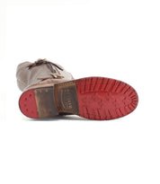 The Bed|Stü Gogo Lug Wide Calf boot lies on its side, displaying its brown leather upper, a distinctive red rubber sole with tread patterns, and brass nails near the heel.