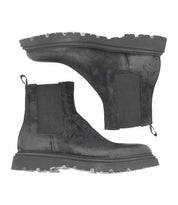 Pair of black men's Grit Chelsea boots by Bed|Stü, featuring thick, rugged soles and elastic side panels, shown from both a side view and a sole view on a white background. These Italian handcrafted boots are designed for both style and durability.