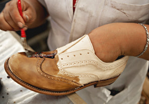 Craftsperson applying finish or dye to a two-tone leather shoe with a small brush.