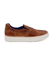 Harry by Bed|Stü: A brown hand-dyed leather slip-on sneaker with a lightweight outsole, white rubber sole, and blue lining, shown from the side against a plain white background.