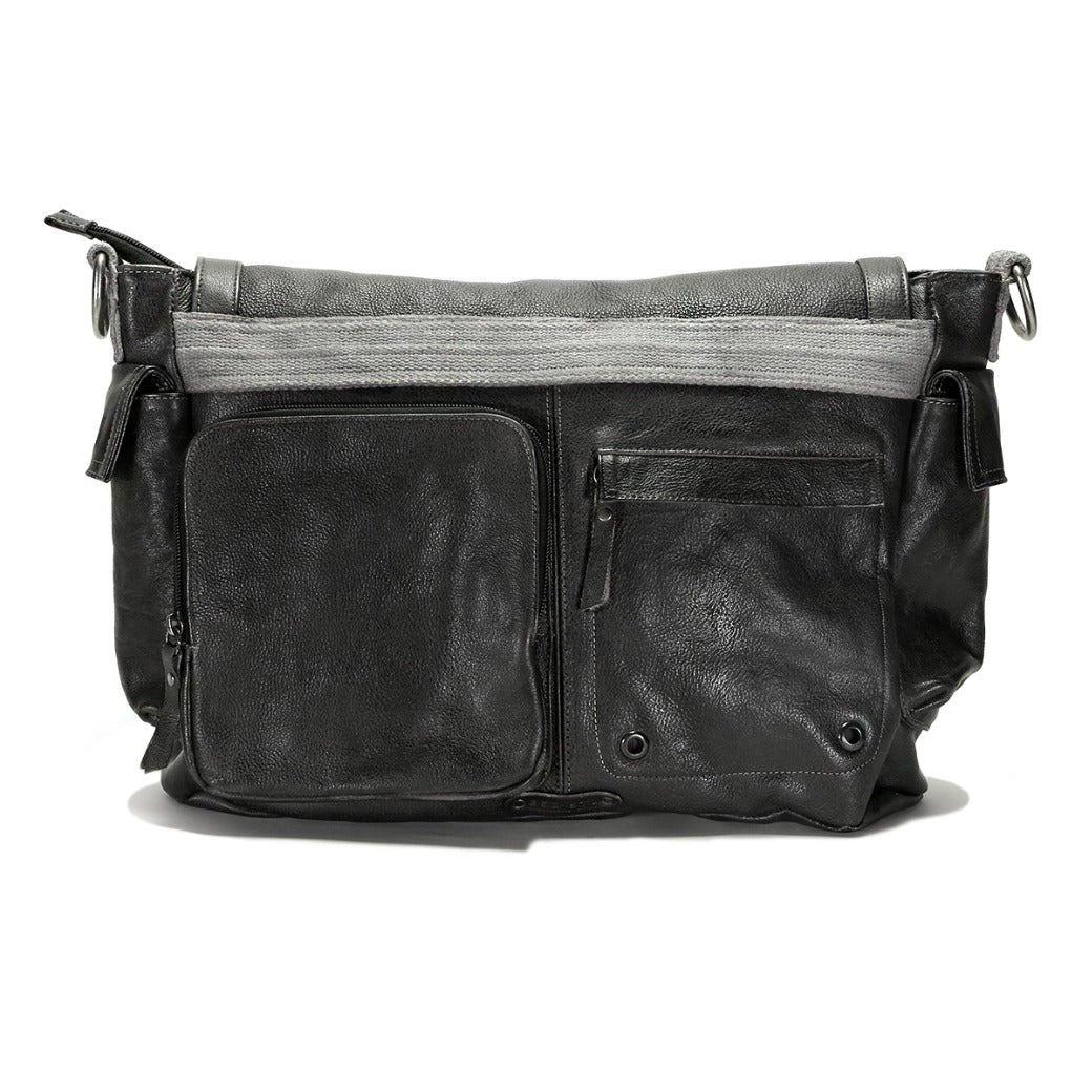 The Bed|Stü Hawkeye II is a large, black leather messenger bag crafted from rugged leather, featuring multiple zippered and flap pockets on the front, silver hardware, a padded laptop sleeve inside, and a gray accent near the top.