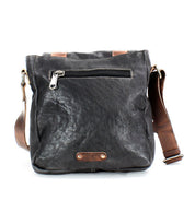 The Hue by Bed|Stü is a black leather crossbody bag featuring a brown adjustable strap, front zipper pocket, and a small metal logo plate at the bottom. With its slightly textured finish and structured yet flexible design, this versatile messenger bag effortlessly transitions from work to weekend.