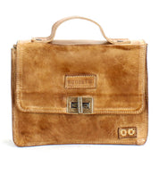 The Bed|Stü Improv is a tan leather briefcase featuring a top handle, front flap secured by two metal clasps, a rectangular embossed logo on the front, and an adjustable crossbody strap for versatile carrying options.