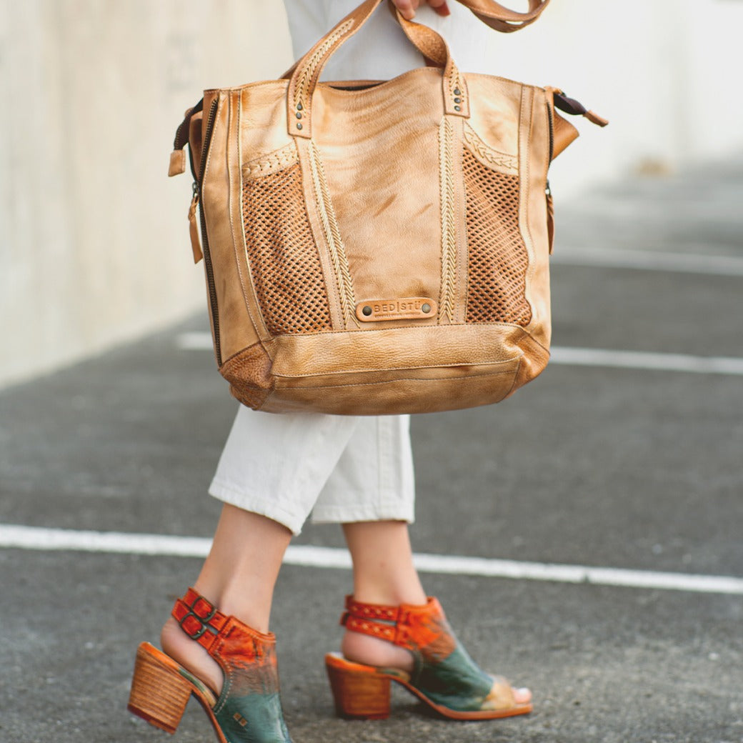 A person walks wearing white pants and multicolored everyday heel sandals, carrying the Bed|Stü Ireni large tan leather tote bag with mesh details.