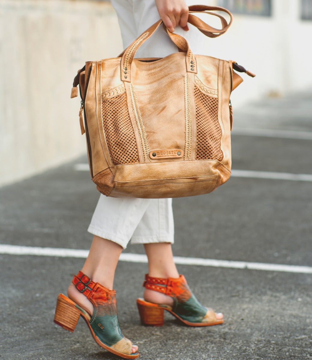 A person walks wearing white pants and multicolored everyday heel sandals, carrying the Bed|Stü Ireni large tan leather tote bag with mesh details.