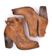 Two Isla ankle boots by Bed|Stü—crafted from smooth brown leather with chunky heels, side zippers, decorative buckles, and an elegant ankle strap—are displayed overlapping on a white background.