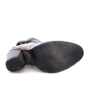 A close-up view of the bottom of a single Bed|Stü Isla bootie showcases its smooth leather construction, worn black sole, block heel, and detailed stitching along the edge. An ankle strap peeks out from above, hinting at the secure fit and timeless style that define this heeled bootie.