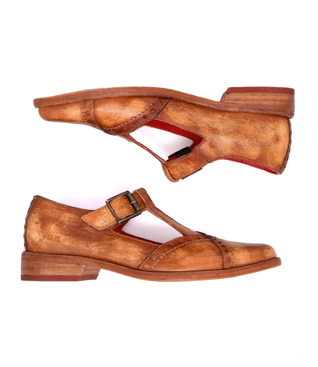 The Bed|Stü Jenny shoes are tan leather T-strap heels featuring a buckle closure, low heel, cushioned insole, and red inner lining, shown against a white background.