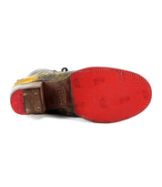 The Bed|Stü Judgement boot is pictured from the bottom, showcasing its bright red sole with visible stitching and embossed text and patterns, along with a distinctive cap toe and a sturdy block heel.