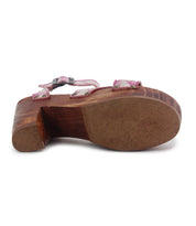 The Bed|Stü Kalah sandal, featuring a thick, sustainably sourced wooden platform heel and pink floral straps, is shown from the bottom to highlight the textured sole and a metal buckle on one adjustable ankle strap.