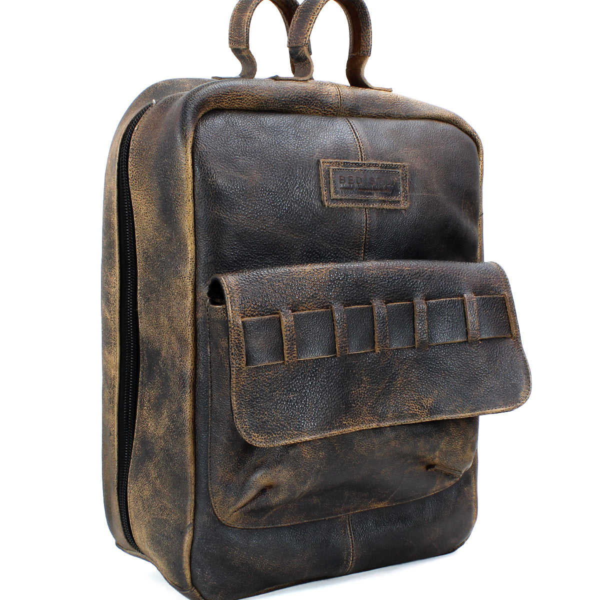 The Bed|Stü Kamet backpack is crafted from brown vegetable-tanned leather and features a front pocket, two top handles, and a zipper closure, all finished in a worn, vintage style.