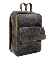 The Bed|Stü Kamet backpack is crafted from brown vegetable-tanned leather and features a front pocket, two top handles, and a zipper closure, all finished in a worn, vintage style.