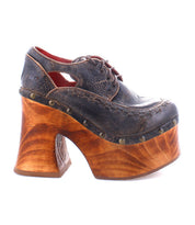 Experience the Bed|Stü Karaoke: a vintage-inspired platform shoe featuring a dark leather upper, decorative stitching, brass studs, lace-up detail, and a chunky sculpted wooden heel reminiscent of classic 70s style.