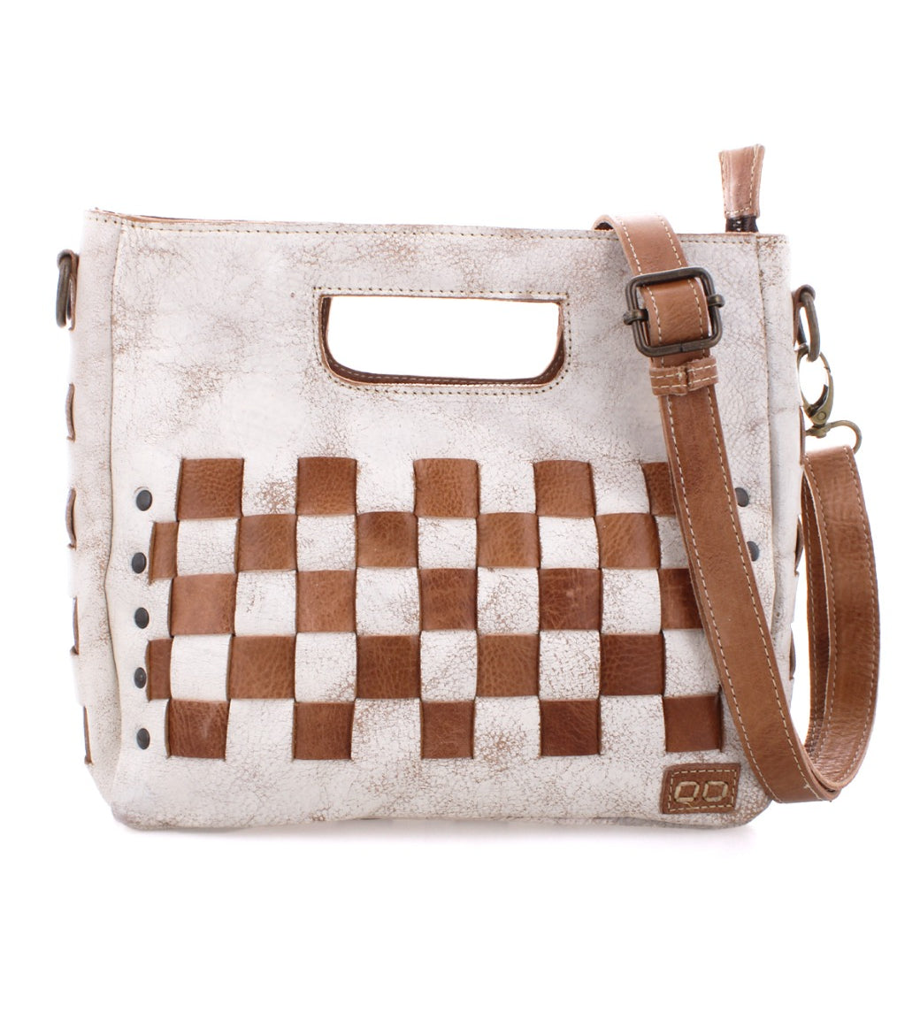 The Keiki crossbody bag by Bed|Stü is crafted from woven leather in a brown and white checkerboard pattern, featuring a cutout handle, zip-top closure, adjustable strap, and decorative metal studs on the front.