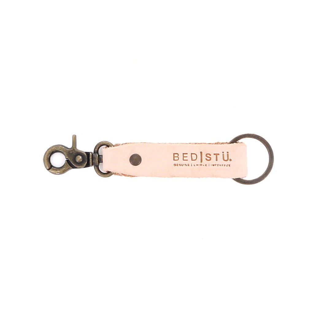 Introducing the Bed|Stü Keygrab: a beige full grain leather keychain with a metal swivel clip and keyring, featuring the Bed|Stü logo and embossed with the words "Genuine | Unique | Imperfect." Perfect as a stylish key organizer.