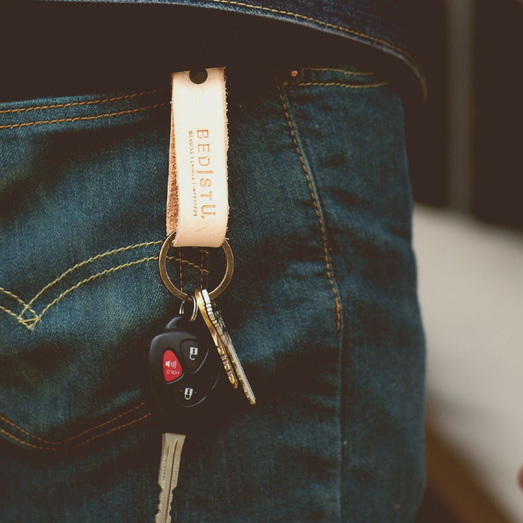 A person wearing jeans has a Bed|Stü Keygrab full grain leather keychain with a swivel clip hanging from their pocket, holding keys and a car remote.