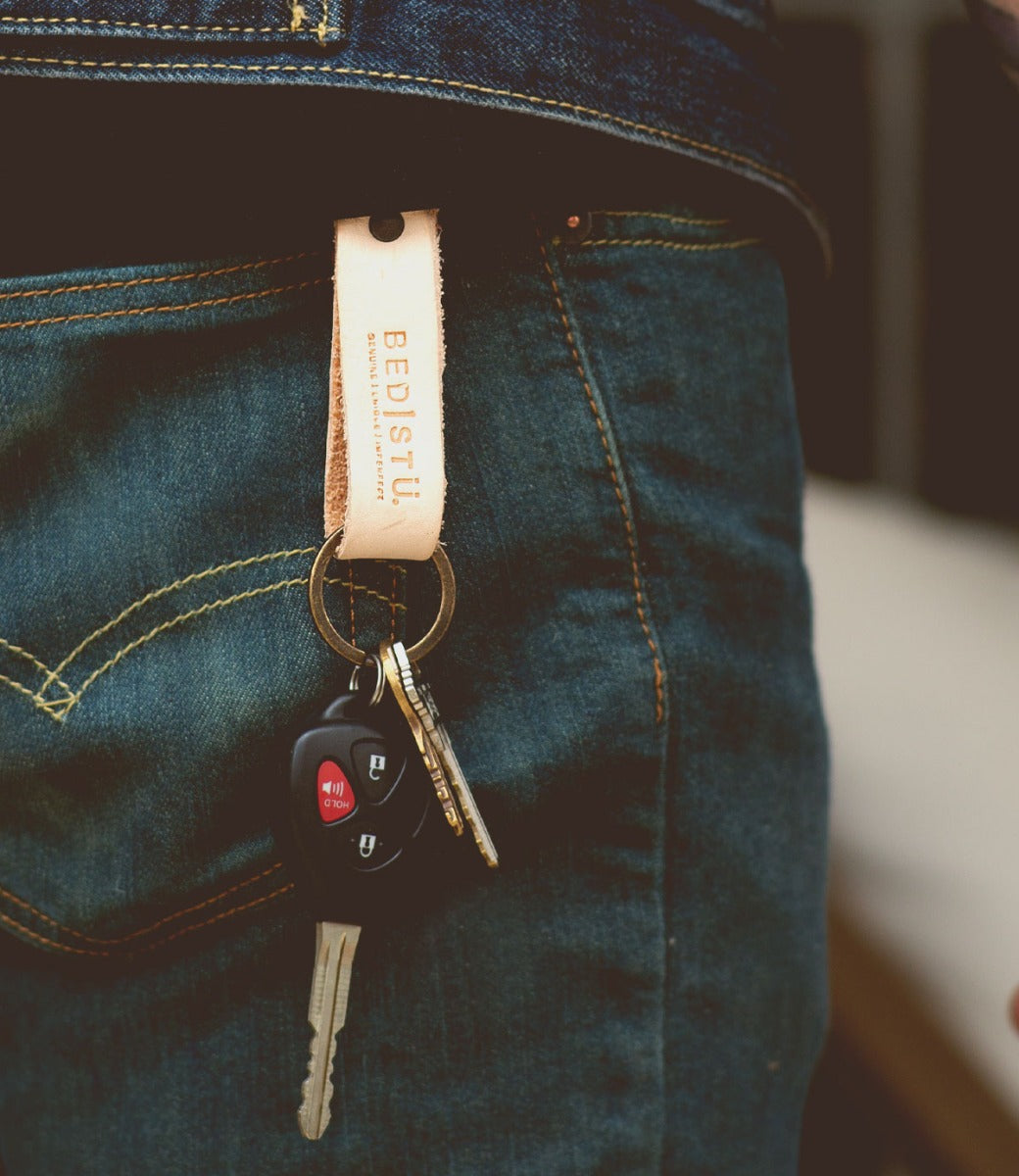 A person wearing jeans has a Bed|Stü Keygrab full grain leather keychain with a swivel clip hanging from their pocket, holding keys and a car remote.
