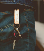 A person wearing jeans has a Bed|Stü Keygrab full grain leather keychain with a swivel clip hanging from their pocket, holding keys and a car remote.
