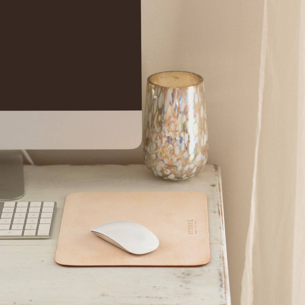 A computer monitor, keyboard, and mouse sit on a white desk next to a marbled glass candle holder, complemented by the Launcher Mouse Pad from Bed|Stü, which elevates this workspace accessory setup.